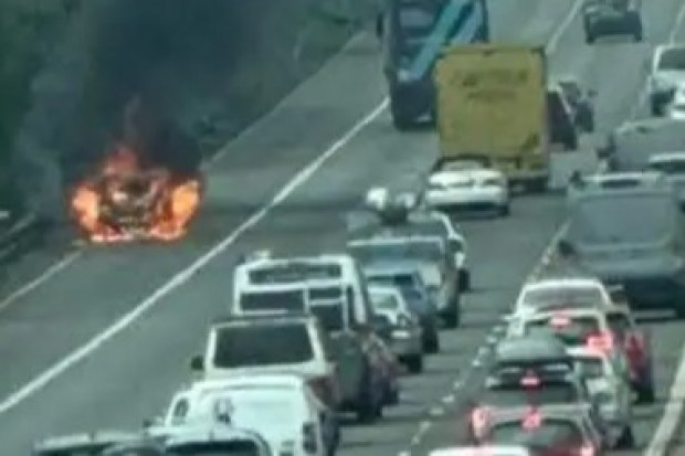 Car engulfed in flames on a highway, causing traffic backup.
