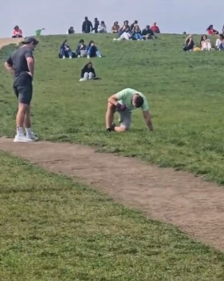 Man vomiting on a grassy hill with spectators.