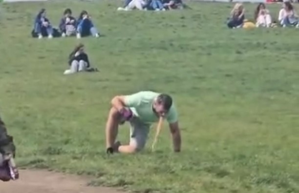 Man vomiting on a grassy hill with people sitting in the background.