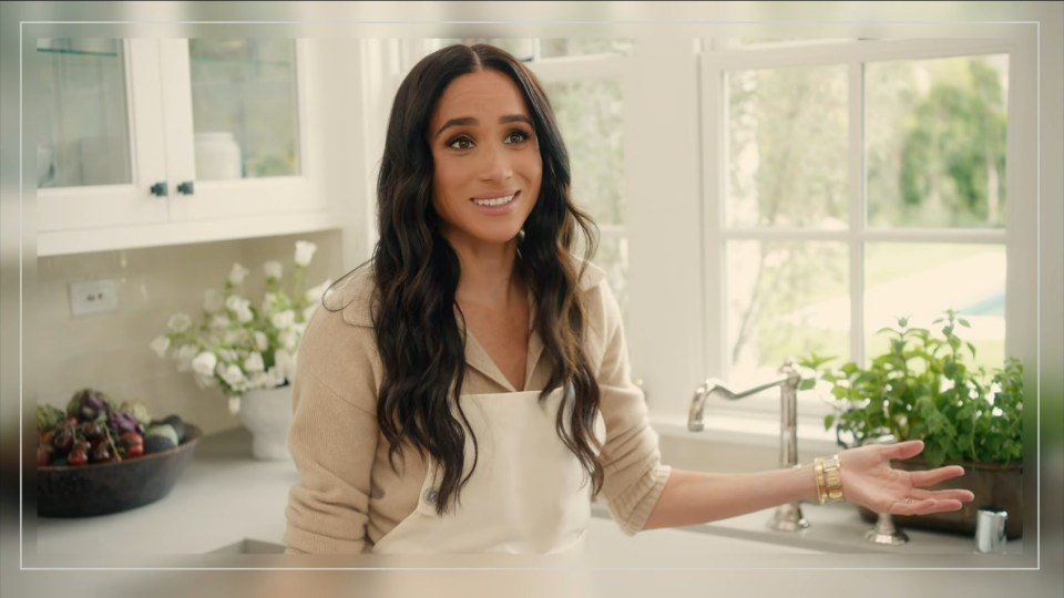 Meghan, Duchess of Sussex, in a kitchen, wearing an apron.
