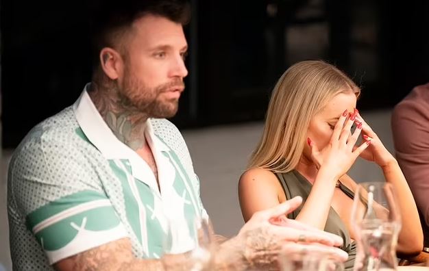 A man and woman sitting at a table, the woman is upset and covering her face with her hands.
