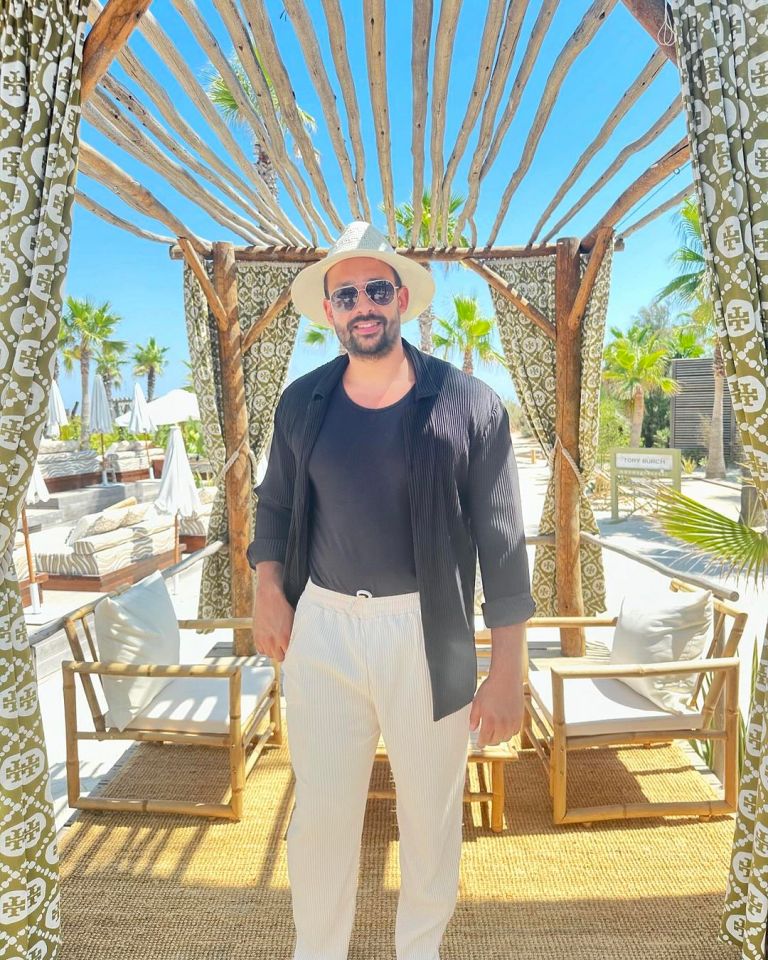 Man in a hat and sunglasses standing in a beachside gazebo.