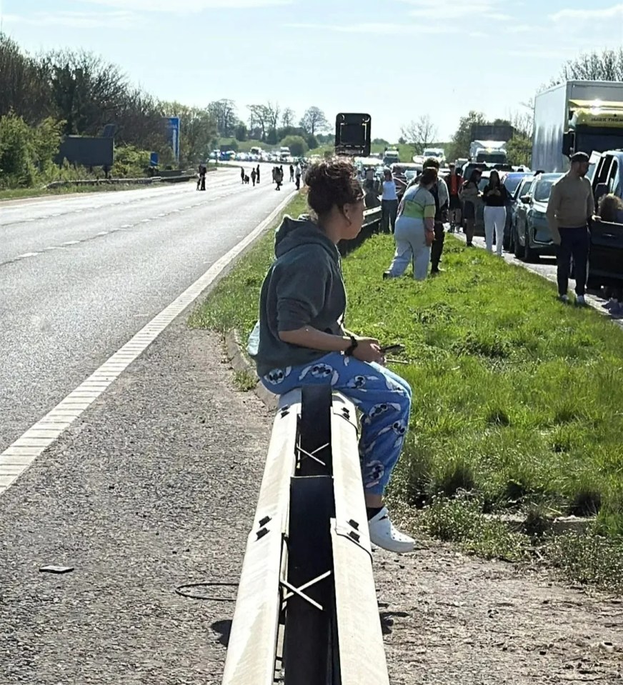 Woman sitting on a highway barrier, traffic jam in the background.