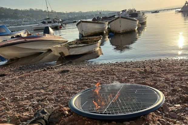 An image collage containing 1 images, Image 1 shows Portable fire pit burning on a beach with boats in the background