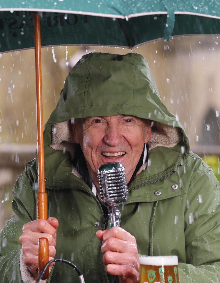 Larry Lamb giving a weather report in a pub garden in the rain.