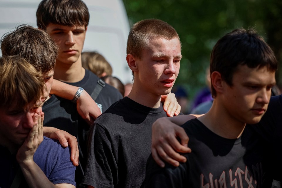 Grieving friends comfort each other at a memorial.