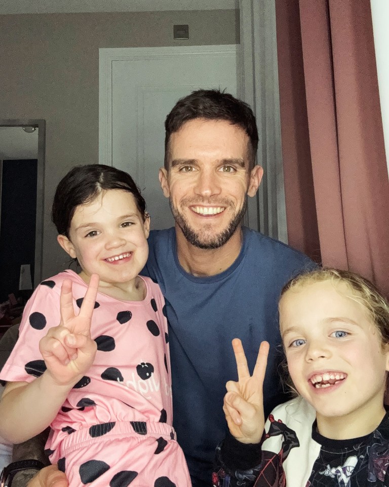 A man poses with two young girls, all making peace signs.
