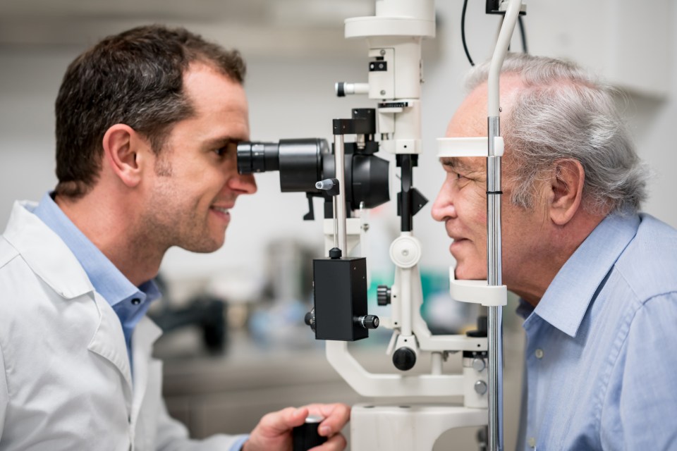 Optometrist performing an eye exam on a senior patient using a phoropter.