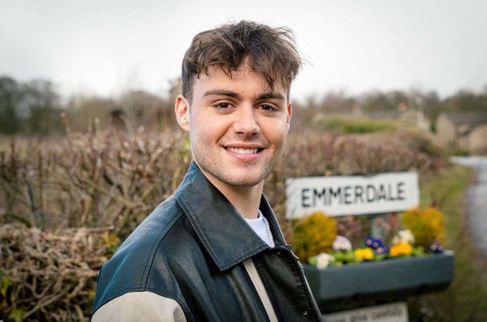 Bradley Riches, Emmerdale star, in front of an Emmerdale sign.