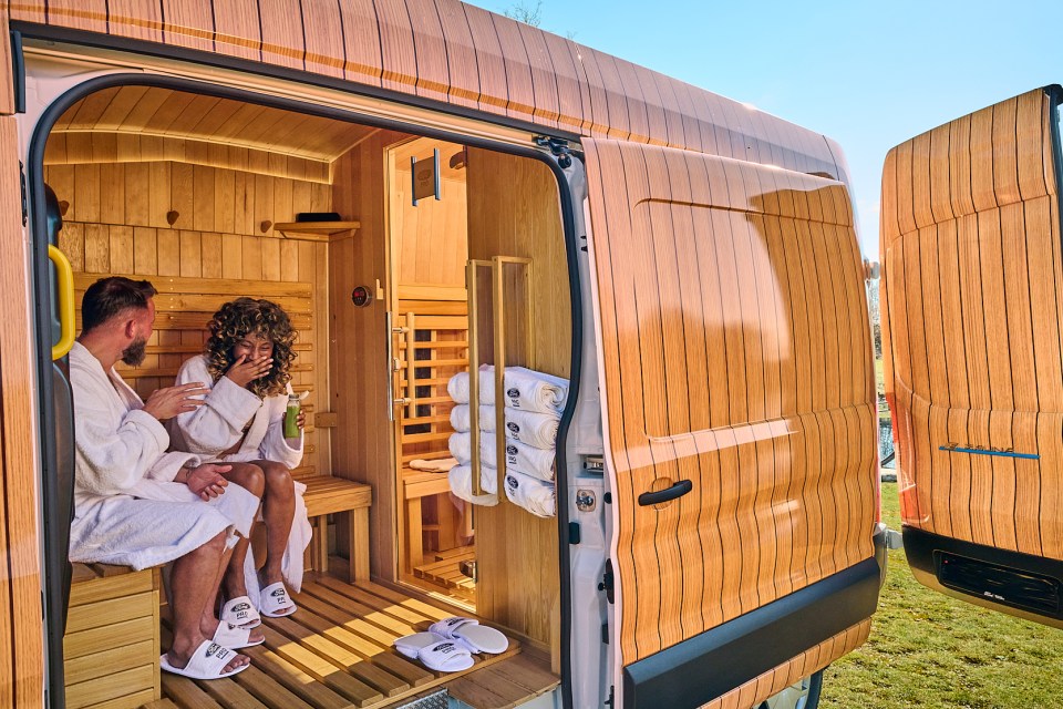 A Ford Transit van converted into a mobile sauna, with two people in robes relaxing inside.
