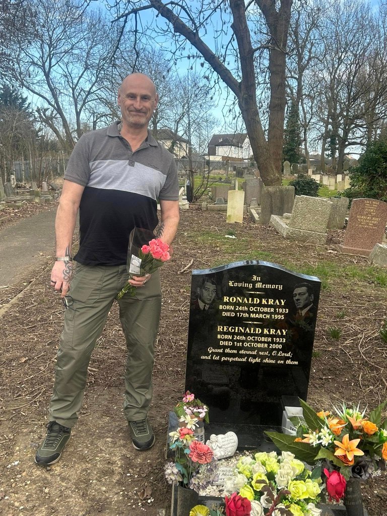 Man visiting the Kray twins' grave with flowers.