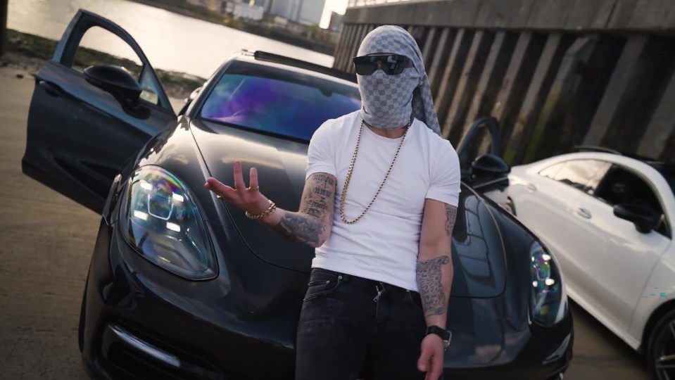 Man in a mask standing between two luxury cars.