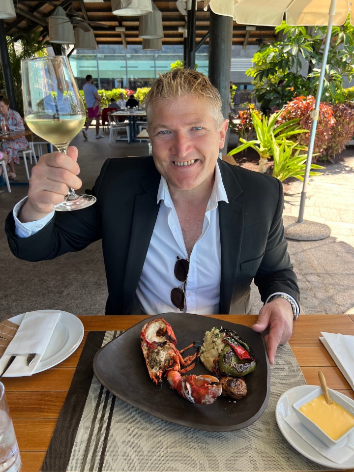 Man in a suit enjoying a grilled lobster meal with a glass of white wine in the Canary Islands.