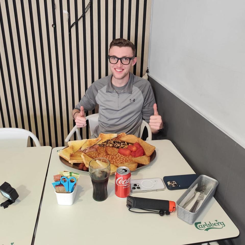 Man giving thumbs up with a large full English breakfast in front of him.