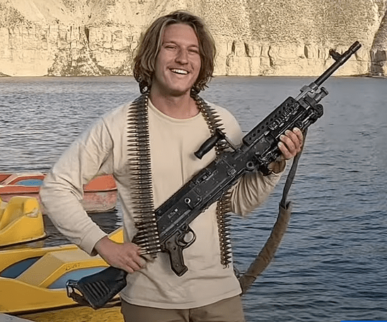 Man holding a machine gun by a body of water.