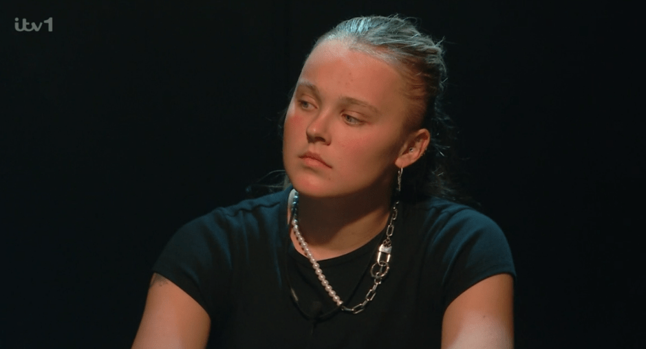 Young woman with serious expression wearing a black shirt and necklaces.