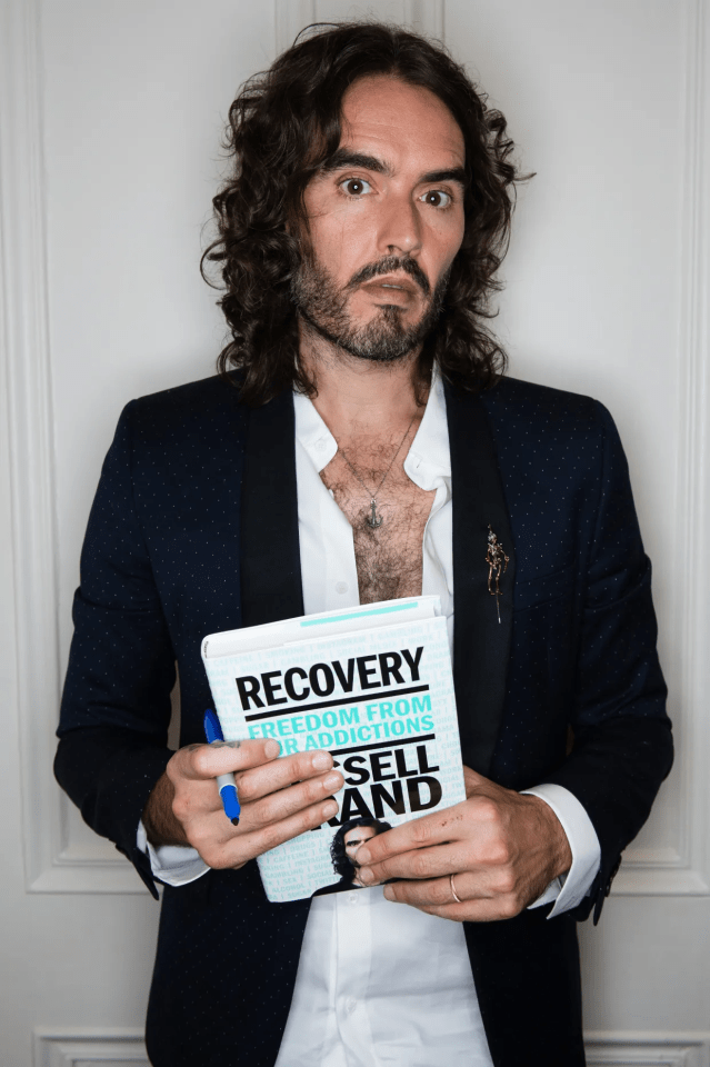 Russell Brand holding his book, "Recovery: Freedom from Our Addictions."