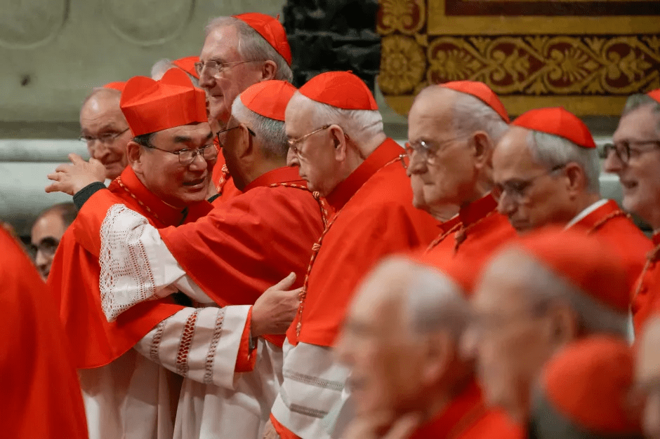 Group of cardinals in red robes embracing.