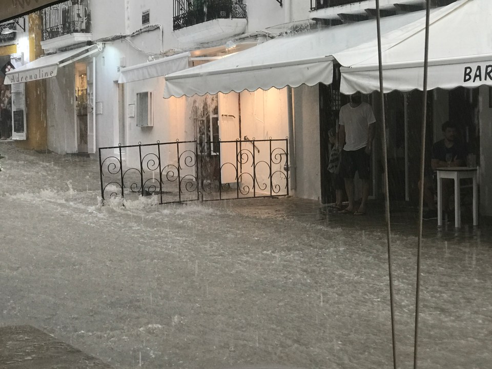 Flooded street scene with people near a bar.