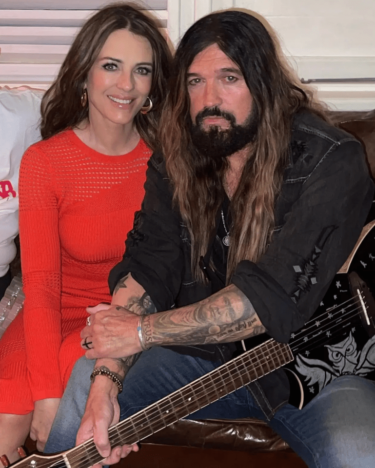 A woman in a red dress sits next to a man with long hair and tattoos, who is holding a guitar.