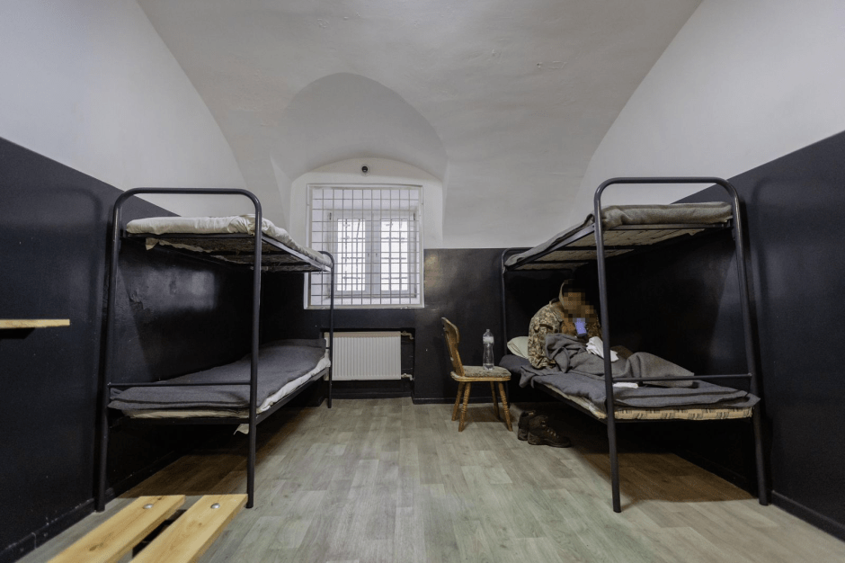 Prison cell with two bunk beds and a person sitting on one of the beds.