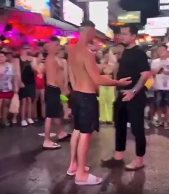 Two shirtless men confronting a man in a crowd.