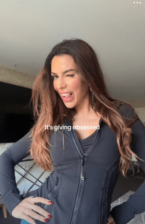 Woman winking and posing in a dark zip-up jacket.  Text overlay reads "It's giving obsessed".