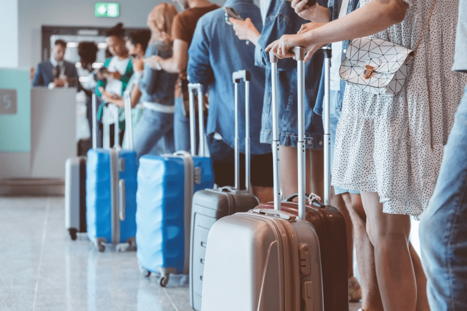 Passengers waiting in line with their luggage at an airport.