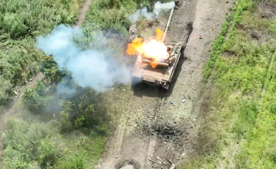 Aerial view of a tank firing, with smoke and flames.