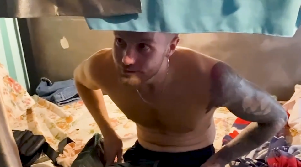 Shirtless man looking down, packing clothes.