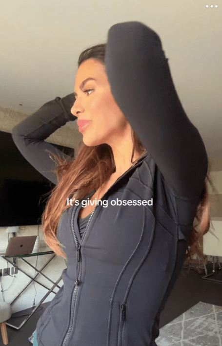 Woman in dark zip-up jacket adjusting her hair.