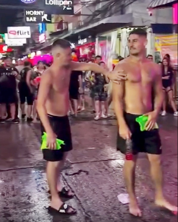 Two shirtless men on a street at night.