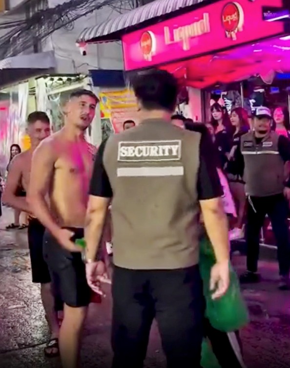 Security guard speaking to shirtless man outside bar.