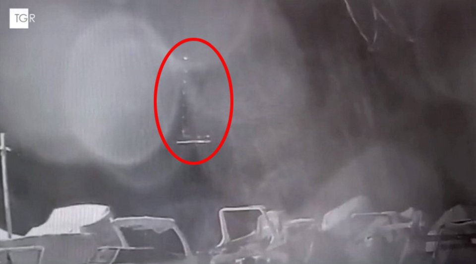 Low-light security camera footage showing an object in the sky above a parking lot.
