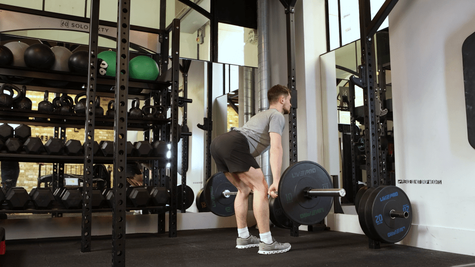 Man performing a barbell deadlift in a gym.