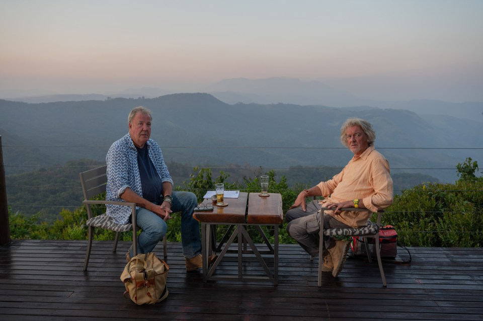 Jeremy Clarkson and James May sitting at a table overlooking a mountain range.