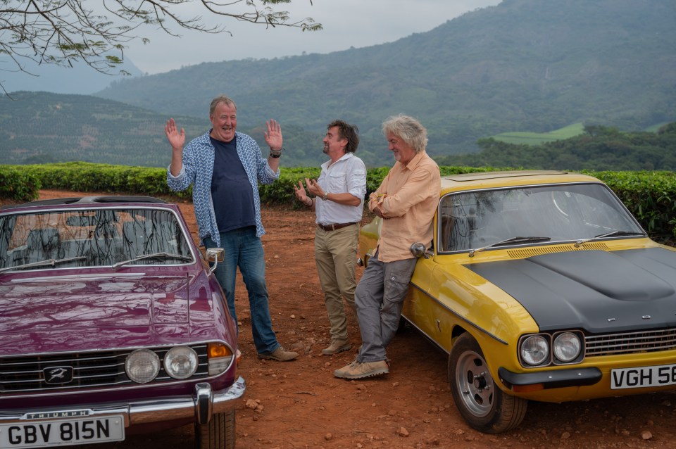 Jeremy Clarkson, Richard Hammond, and James May standing by classic cars.