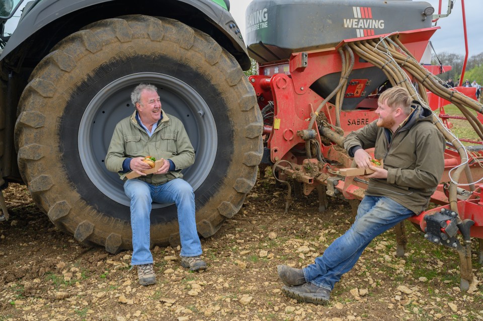 Two men eating lunch near farm equipment.