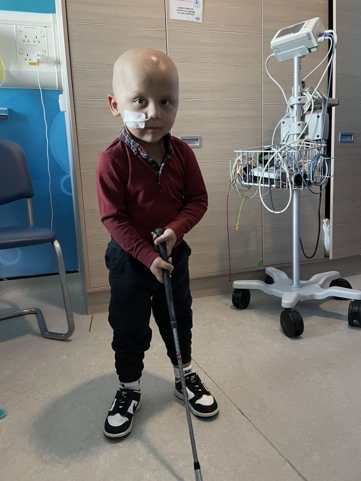 A young boy with leukemia holds a golf club in a hospital room.