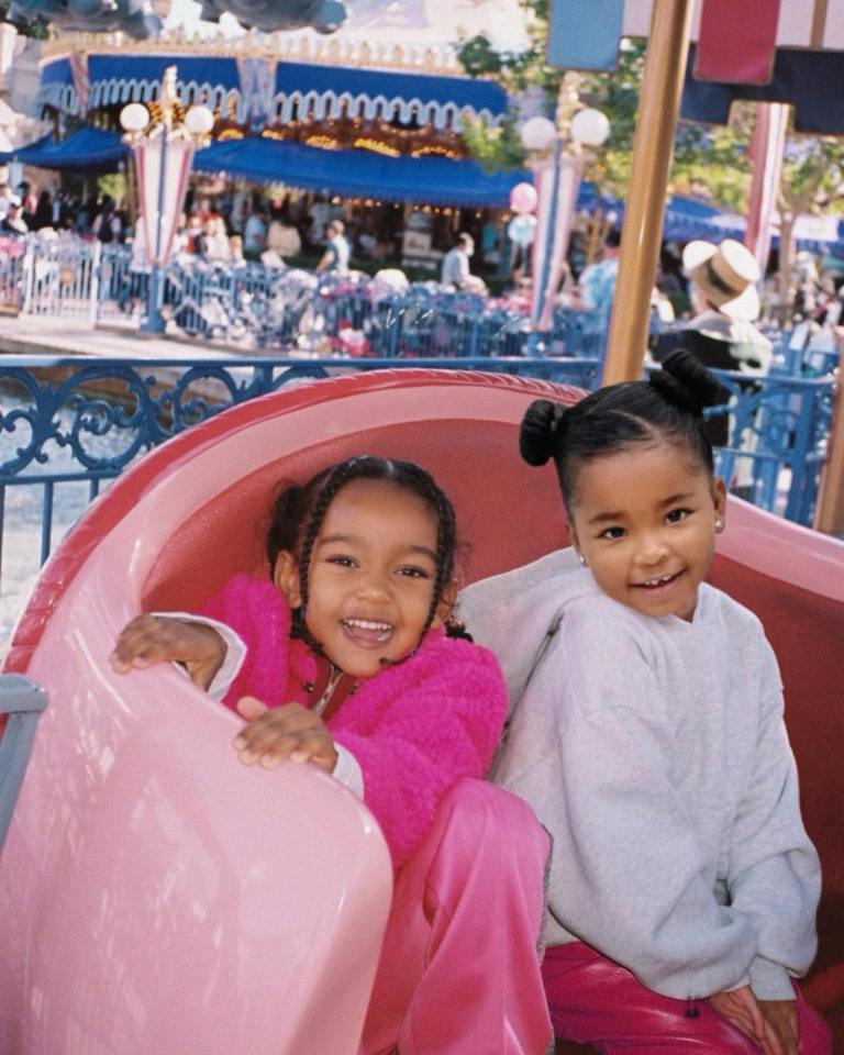Two young girls on a pink carousel ride at an amusement park.