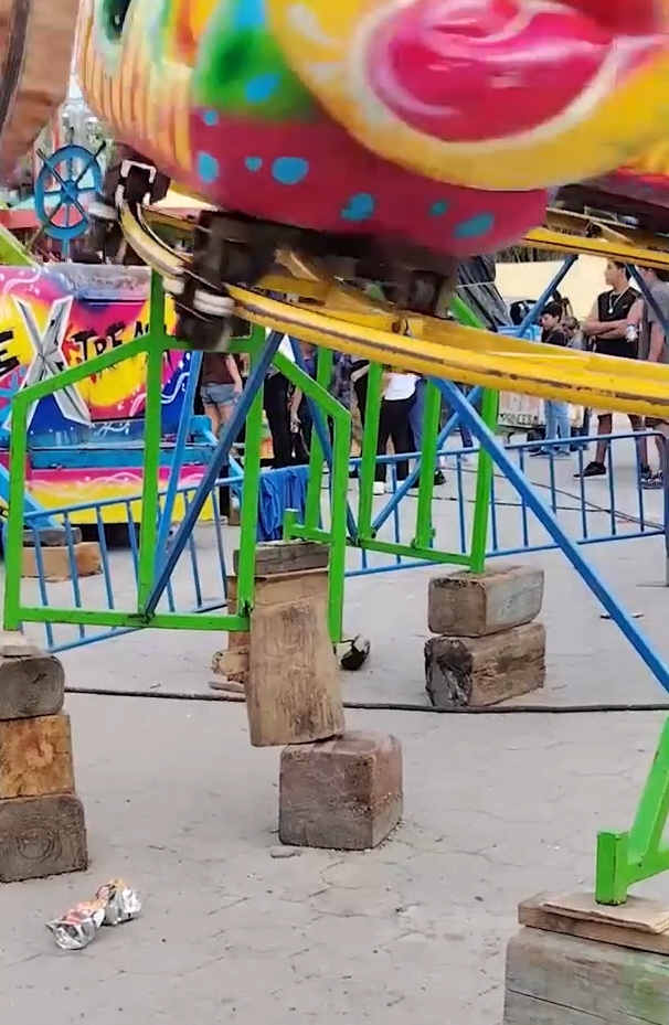 Children's fairground ride precariously supported by wooden blocks.