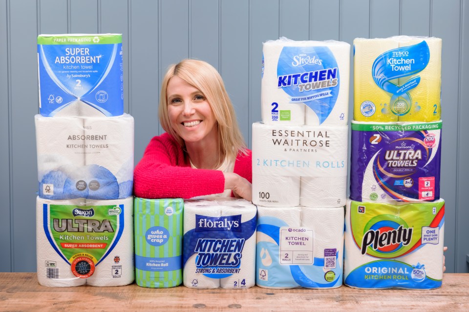 Woman surrounded by various brands of kitchen paper rolls.