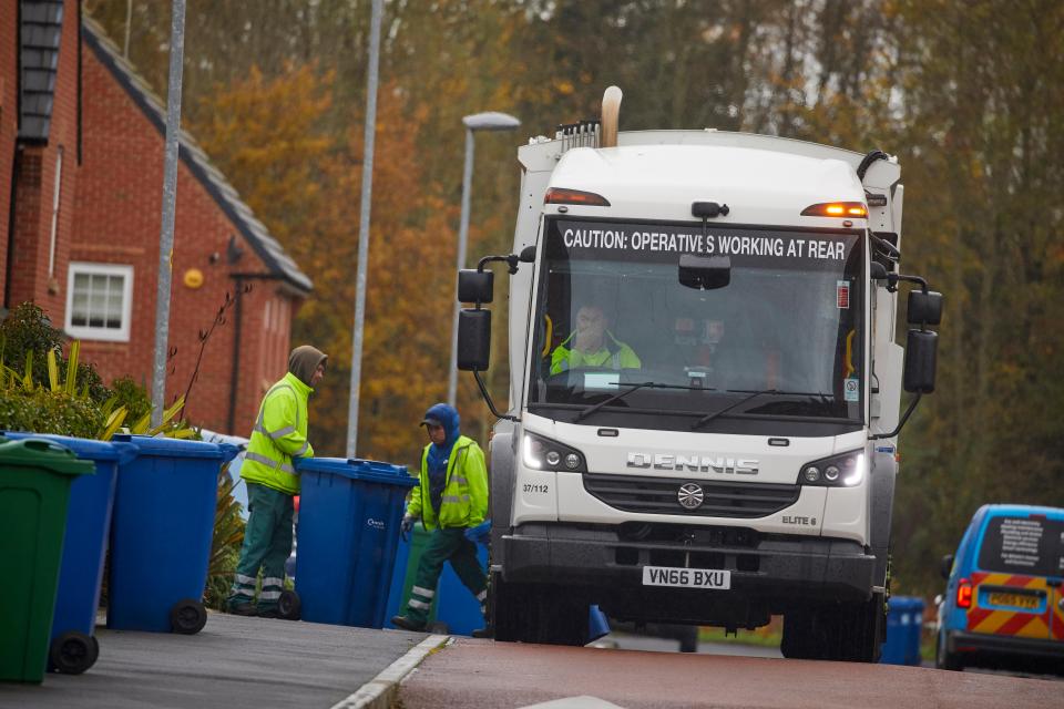 Garbage collectors emptying bins into a refuse truck.