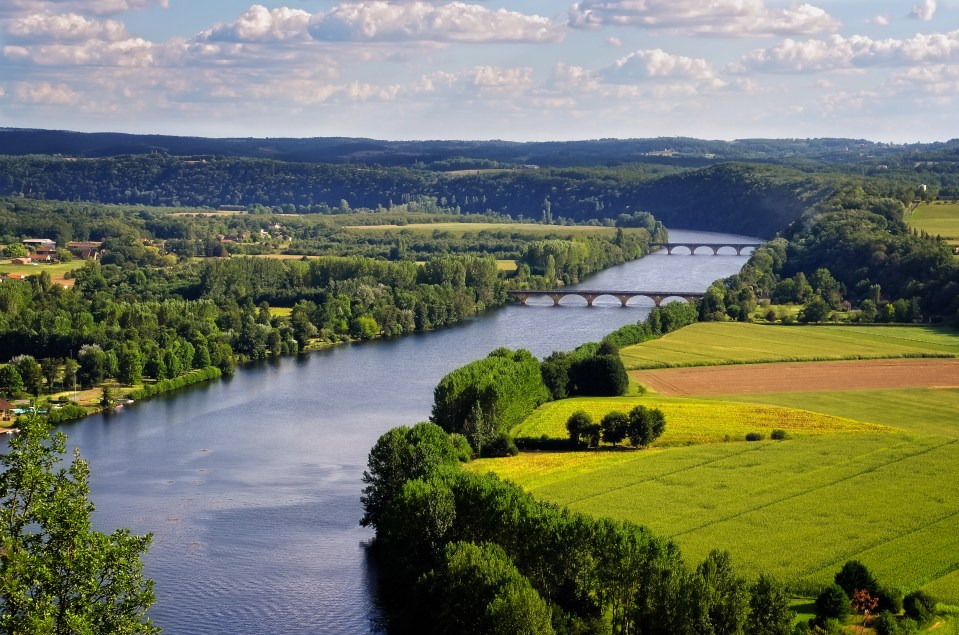 Aerial view of the Dordogne River in France, with a bridge and surrounding landscape.