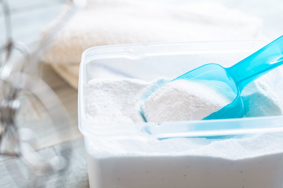 Laundry detergent powder in a plastic container with a blue scoop.