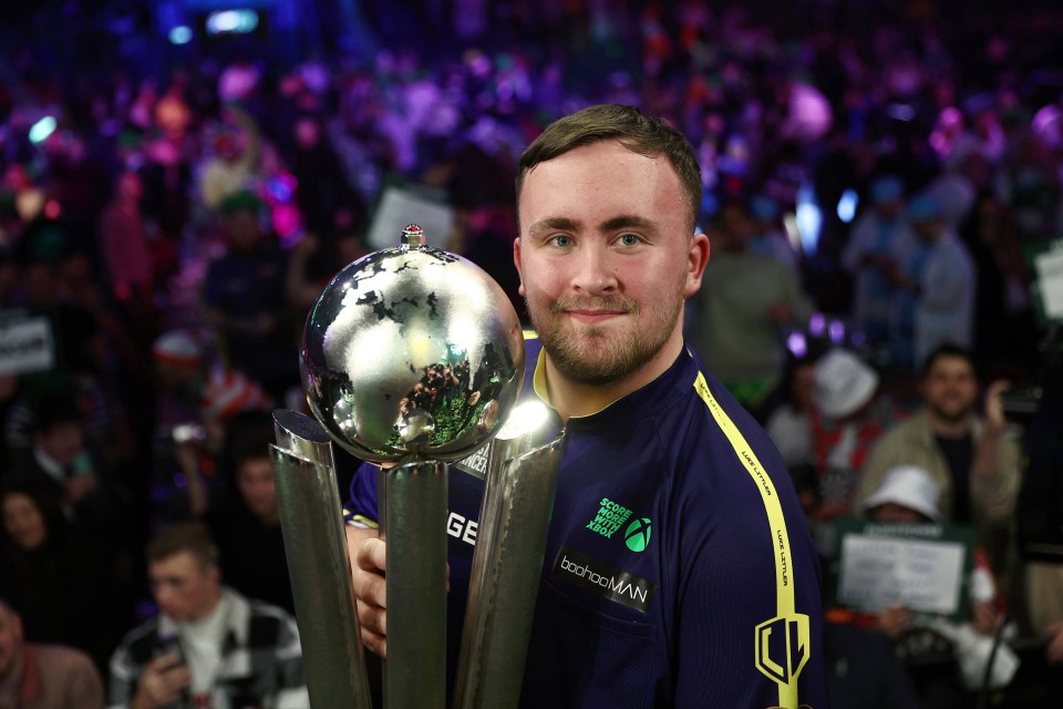 Luke Littler holding the Sid Waddell Trophy after winning a darts championship.