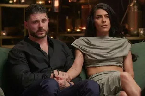 A man and woman sitting on a couch, holding hands.