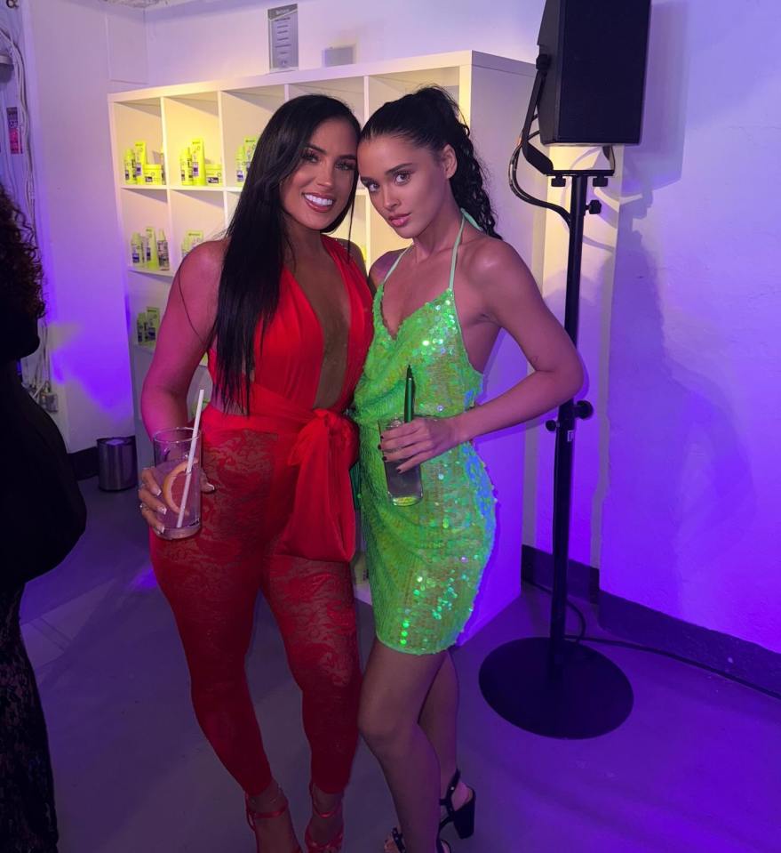 Two women posing together at an event, one in a red jumpsuit and the other in a lime green sequined dress.