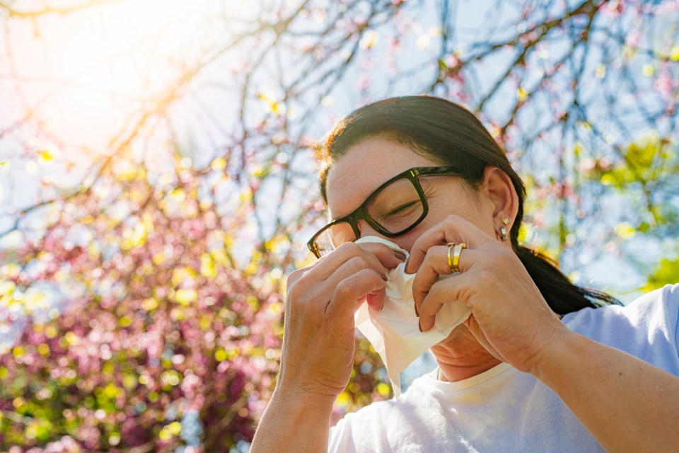 Woman blowing her nose with a tissue outdoors in spring.