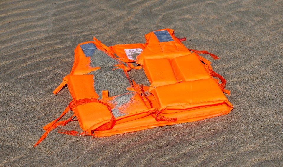 Orange life jacket discarded on a sandy beach.
